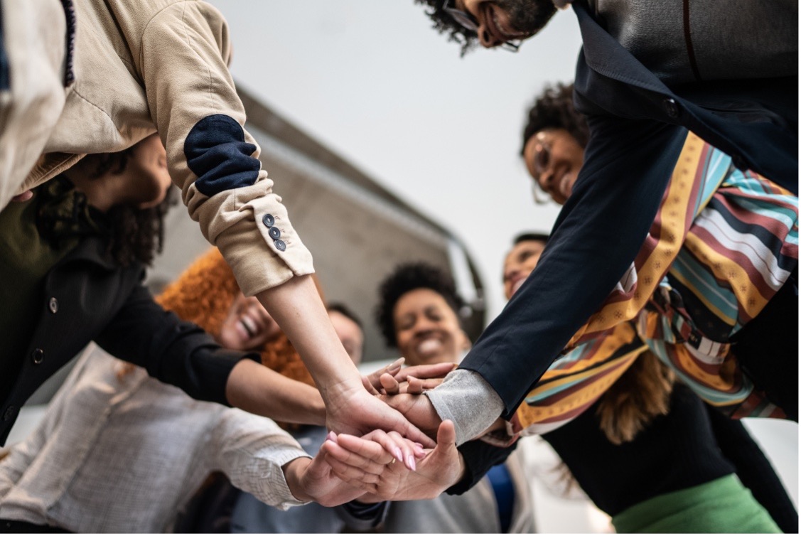 A group of people standing in a circle and placing their hands together in the center