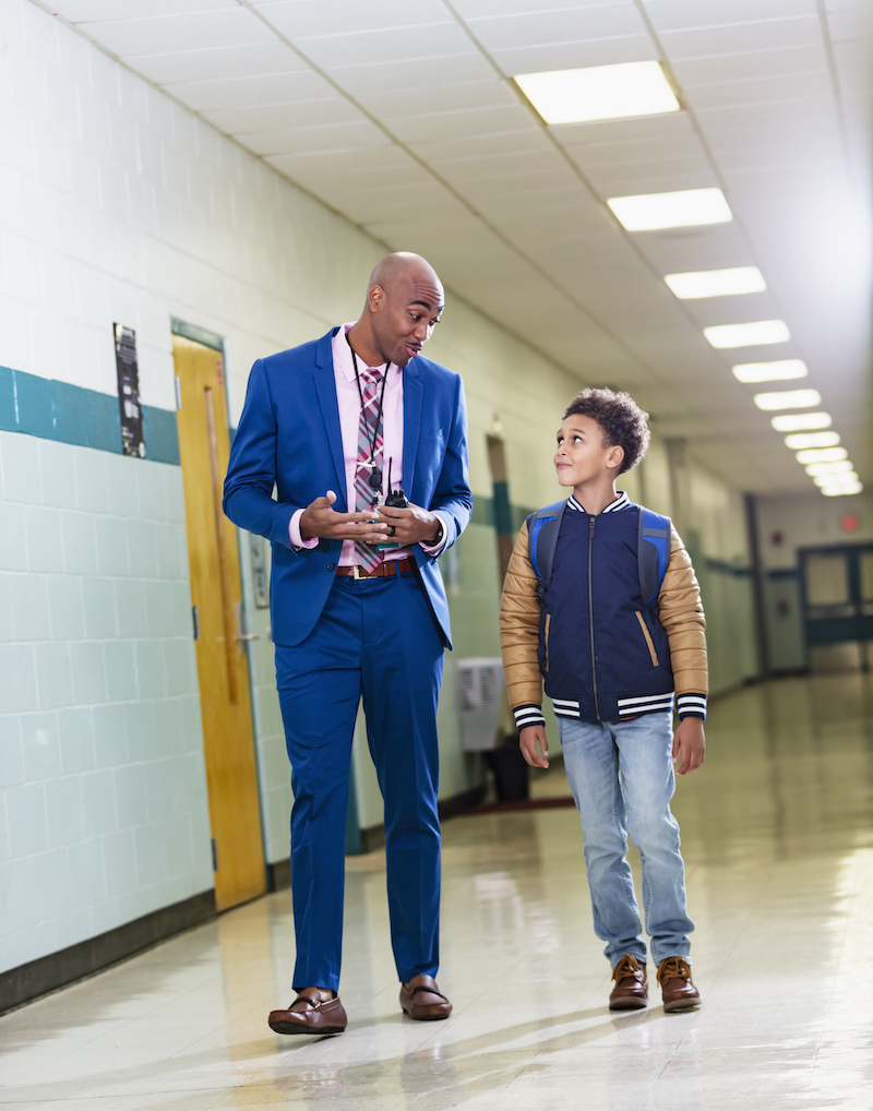 Multiracial student and teacher walking together in school hallway