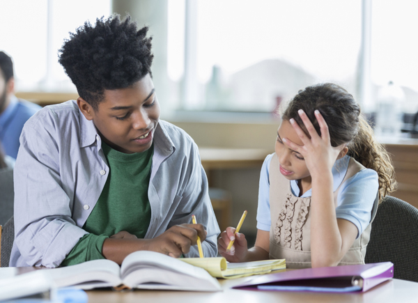 Male high school student helps an elementary school student with a math assignment