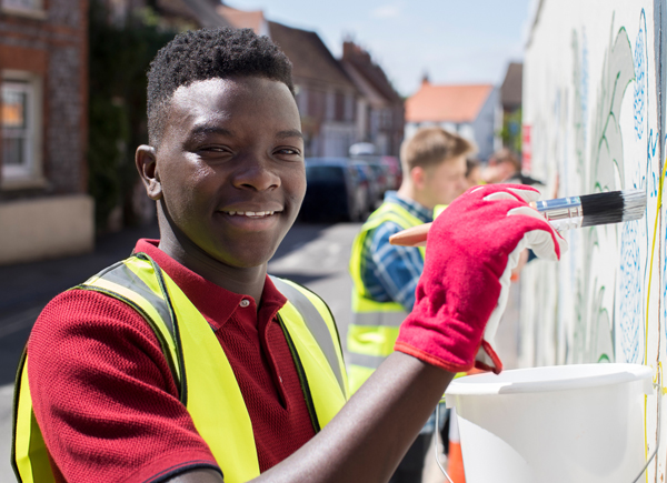 Image of a young, smiling African American male painting a wall