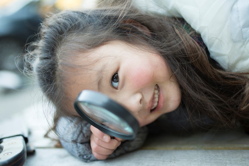 Young girl smiles as she looks through a magnifying glass