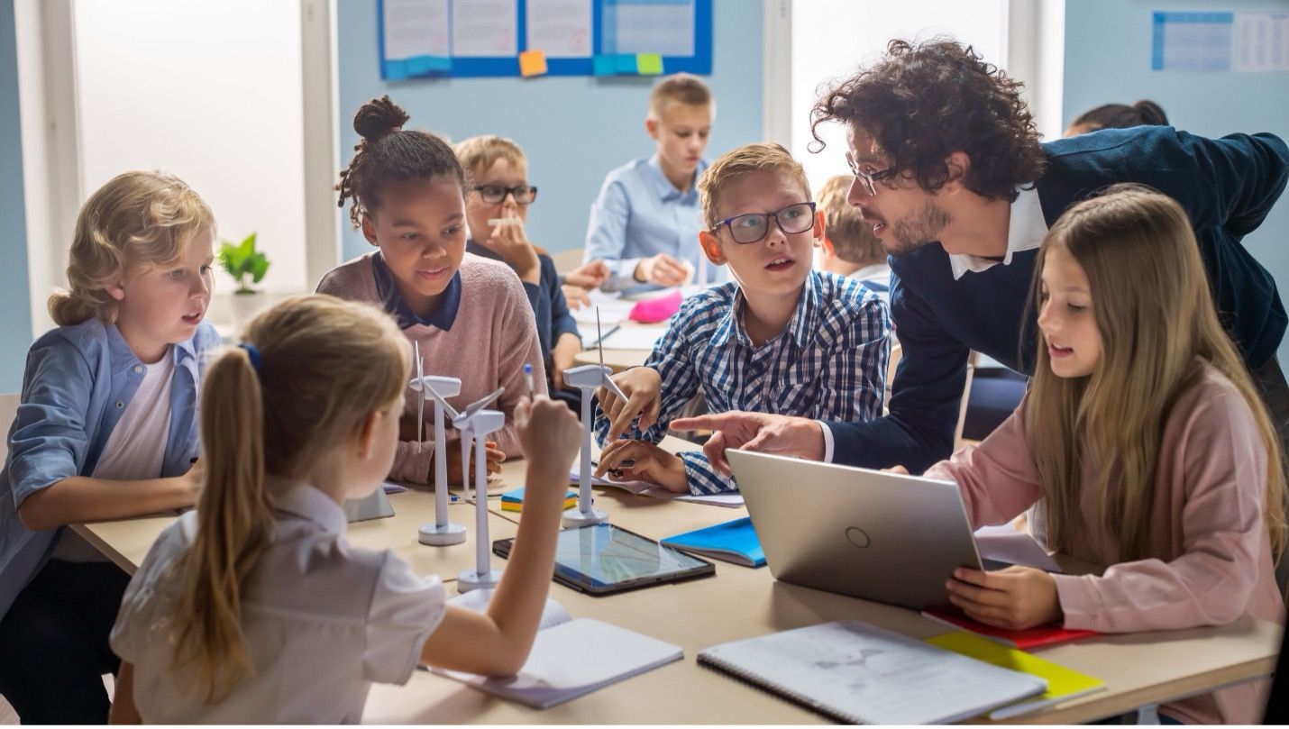 Teacher interacting with students working on wind turbine models in a classroom.